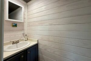 Small Mount Meadow Lane bathroom sink with a mirror above, soap dispenser, and white wood panel walls.