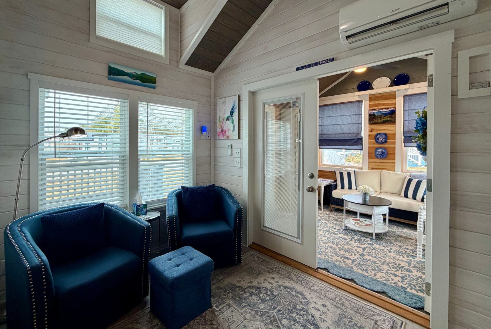 Cozy living room on Mount Meadow Lane with blue chairs, ottoman, and decor, next to a sunlit patio with blue accents.