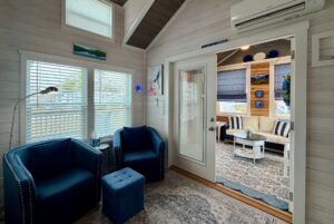 Cozy living room on Mount Meadow Lane with blue chairs, ottoman, and decor, next to a sunlit patio with blue accents.
