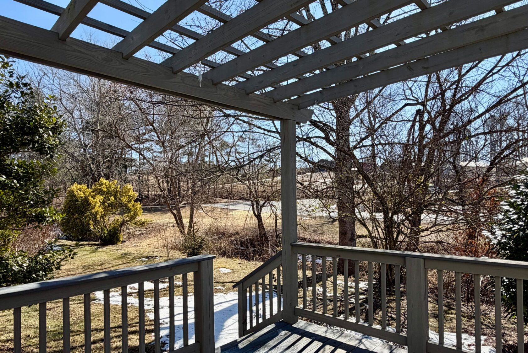 View from a wooden porch at 139 Drifting Brook, overlooking a yard with leafless trees and patches of snow.