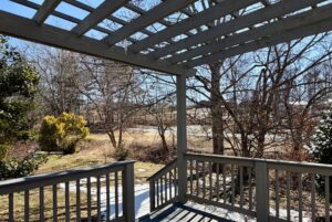 View from a wooden porch at 139 Drifting Brook, overlooking a yard with leafless trees and patches of snow.