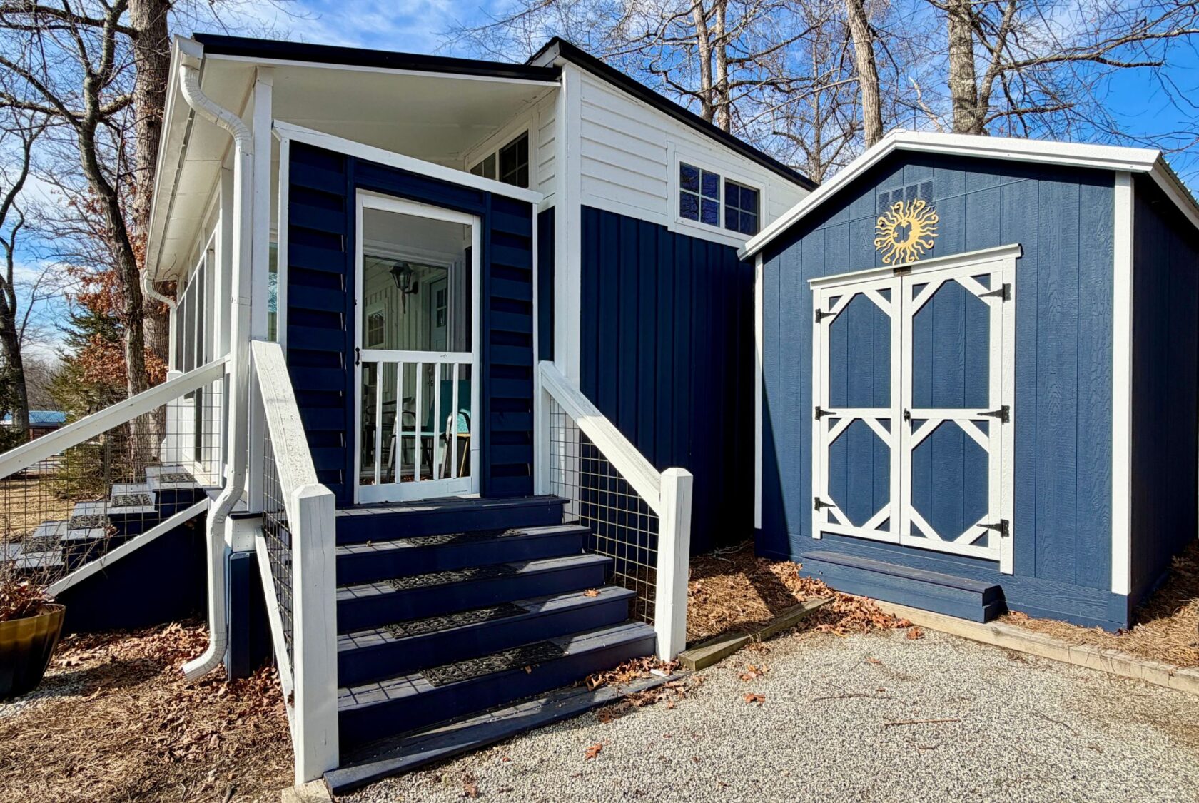 A blue tiny house with white trim on Empire Lane, plus a matching blue shed adorned with a sun decoration.