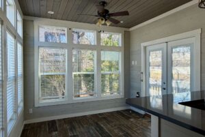 Bright sunroom with large windows, wood floors, gray walls, and glass double doors in this 139 Drifting Brook home for sale.