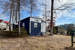 A small blue and white house stands among leafless trees on sunny Empire Lane, with other houses nearby.