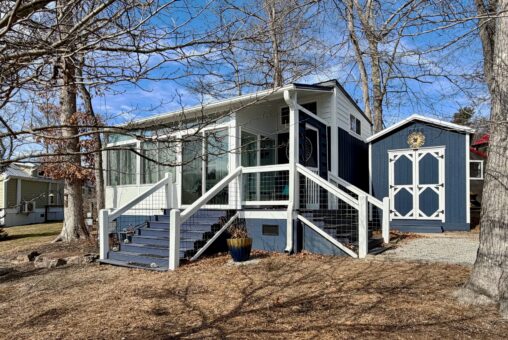 Charming small blue and white house on Empire Lane, with a front porch, shed, and sunny leafless trees.