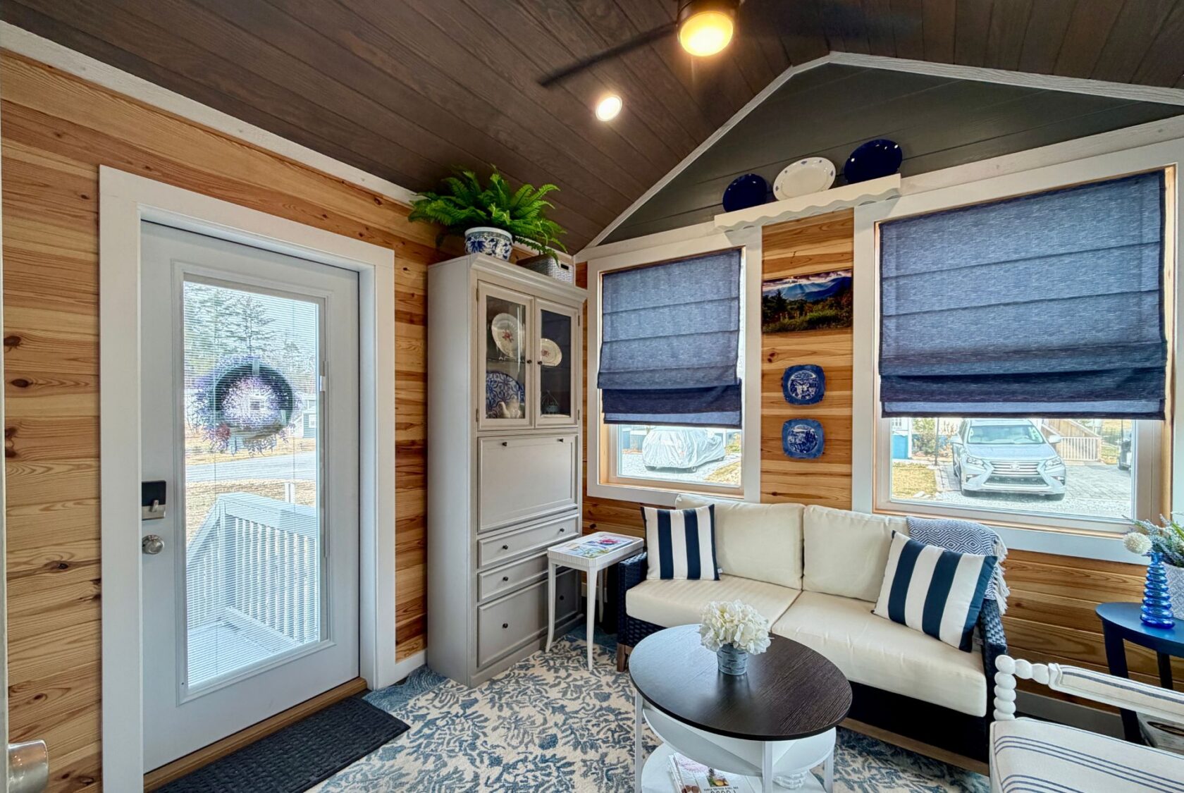 Cozy Mount Meadow Lane living room with blue decor, white sofa, cabinet, round table, and large windows with blue shades.
