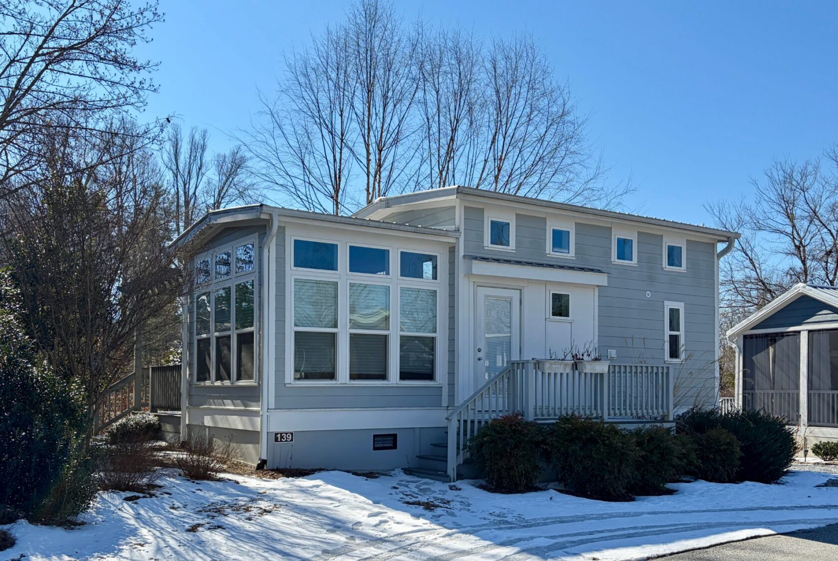 Charming small gray house on Drifting Brook Lane, with many windows, porch, and light snow under a clear sky.