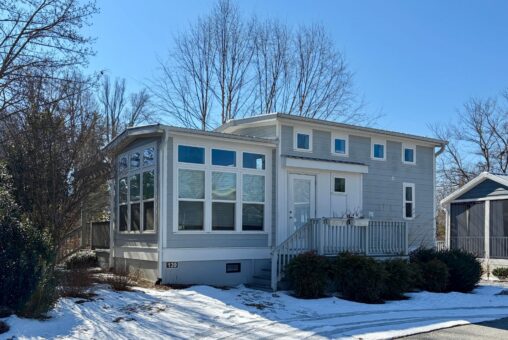 Charming small gray house on Drifting Brook Lane, with many windows, porch, and light snow under a clear sky.