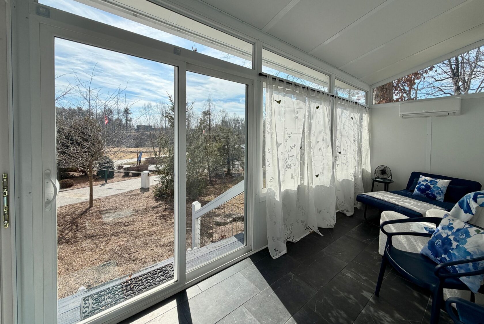 A sunroom on Empire Lane with sheer curtains, black tile floor, and an outdoor view through glass doors.
