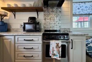 Modern kitchen at 5 Empire Lane with beige cabinets, stove, microwave, open shelves, and a decorative tile backsplash.