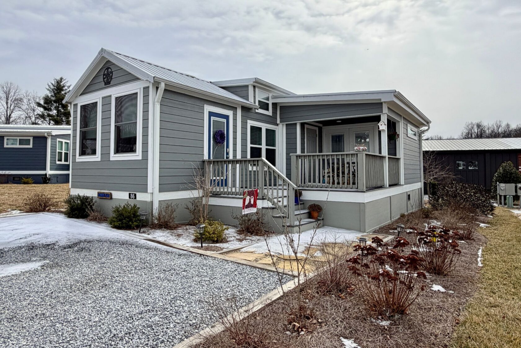 A small gray house with a porch on Mount Meadow Lane, winter plants, and patches of snow on the ground and driveway.
