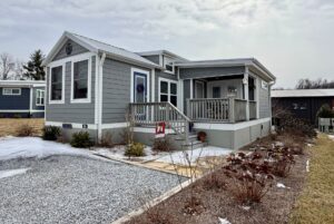 A small gray house with a porch on Mount Meadow Lane, winter plants, and patches of snow on the ground and driveway.