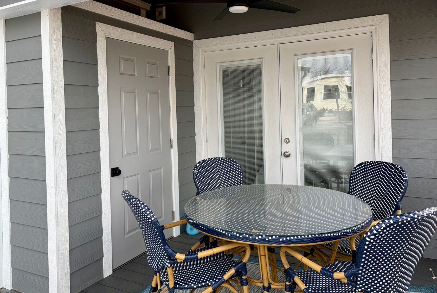 Round glass table with four blue patterned chairs on the porch at Mount Meadow Lane, next to gray and white doors.