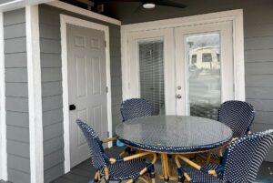 Round glass table with four blue patterned chairs on the porch at Mount Meadow Lane, next to gray and white doors.