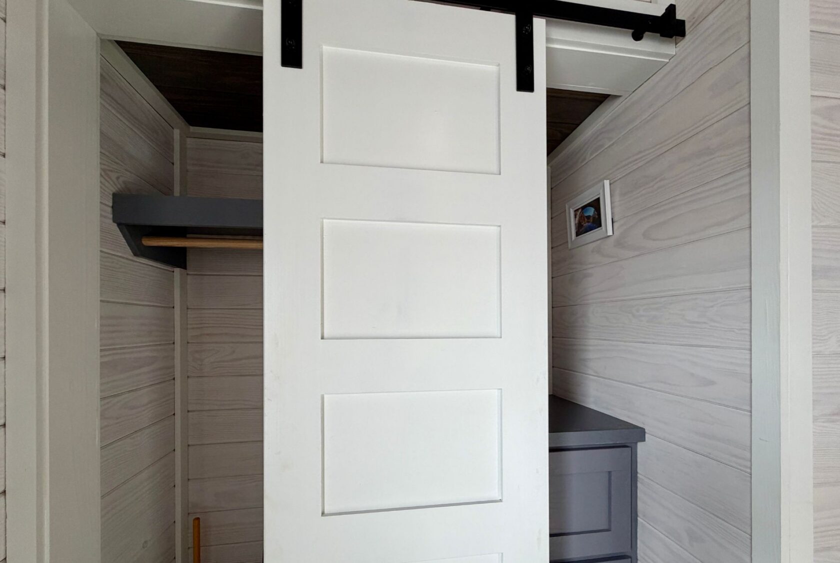 White sliding barn door halfway open on Mount Meadow Lane, revealing a small closet with shelves and a framed photo.