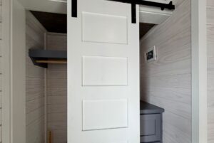 White sliding barn door halfway open on Mount Meadow Lane, revealing a small closet with shelves and a framed photo.