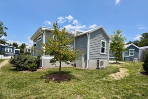 A small gray house with white trim and a young tree sits on Mount Meadow Lane under a blue, cloud-streaked sky.