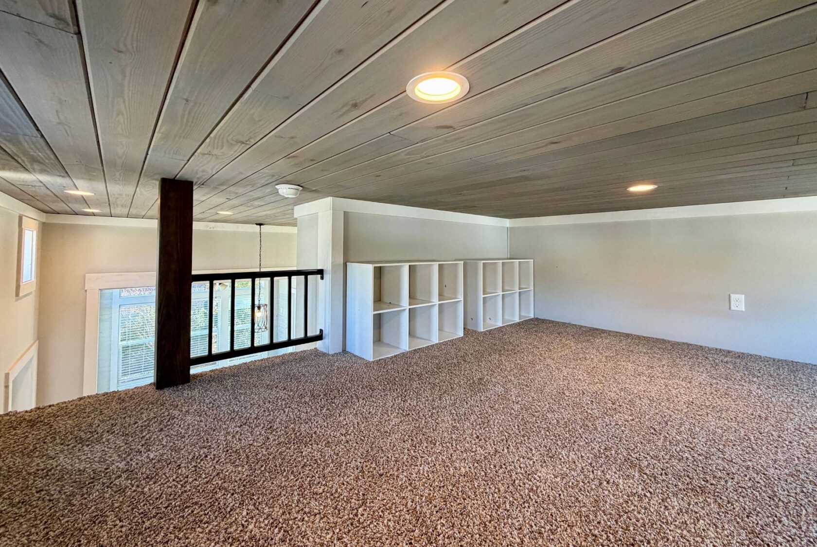 Carpeted loft at 139 Drifting Brook Lane with cubby shelves, wood ceiling, and railing overlooking windows below.
