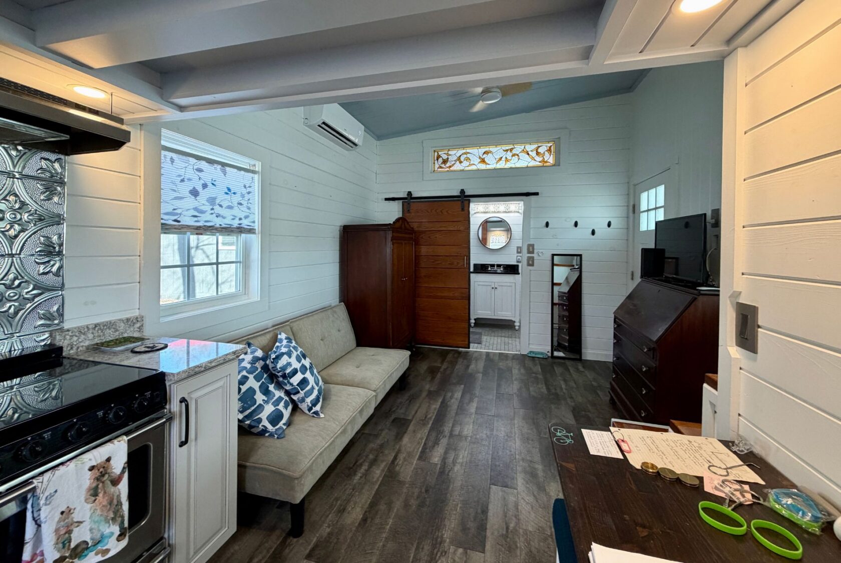 A cozy, modern tiny house interior by Empire Lane with a sofa, kitchen, wooden floor, and view into the bathroom.