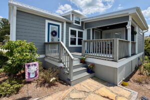 Gray house on Mount Meadow Lane with a small porch, blue door, potted plants, and a decorative flag in the yard.