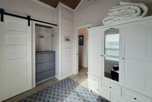 Bright bedroom on Mount Meadow Lane with white paneled walls, blue dresser, rug, and linens atop the closet.