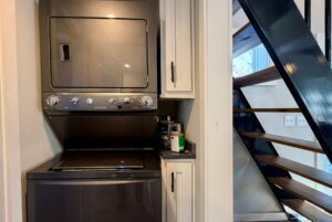 Stacked washer and dryer in a laundry nook at 139 Drifting Brook Lane by the modern black metal staircase.