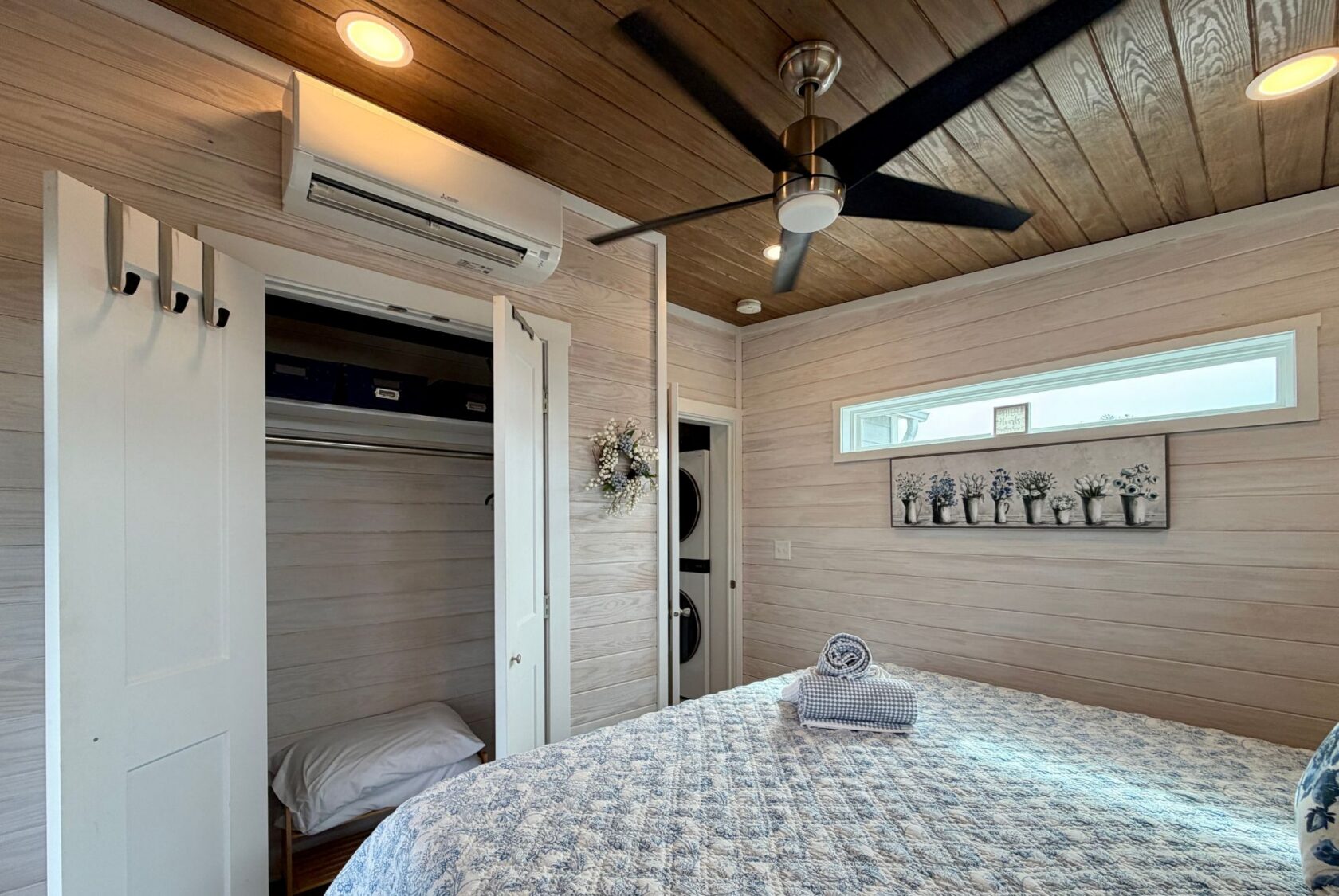 Cozy Mount Meadow Lane bedroom with open closet, ceiling fan, quilted bed, and floral decor on wood-paneled walls.