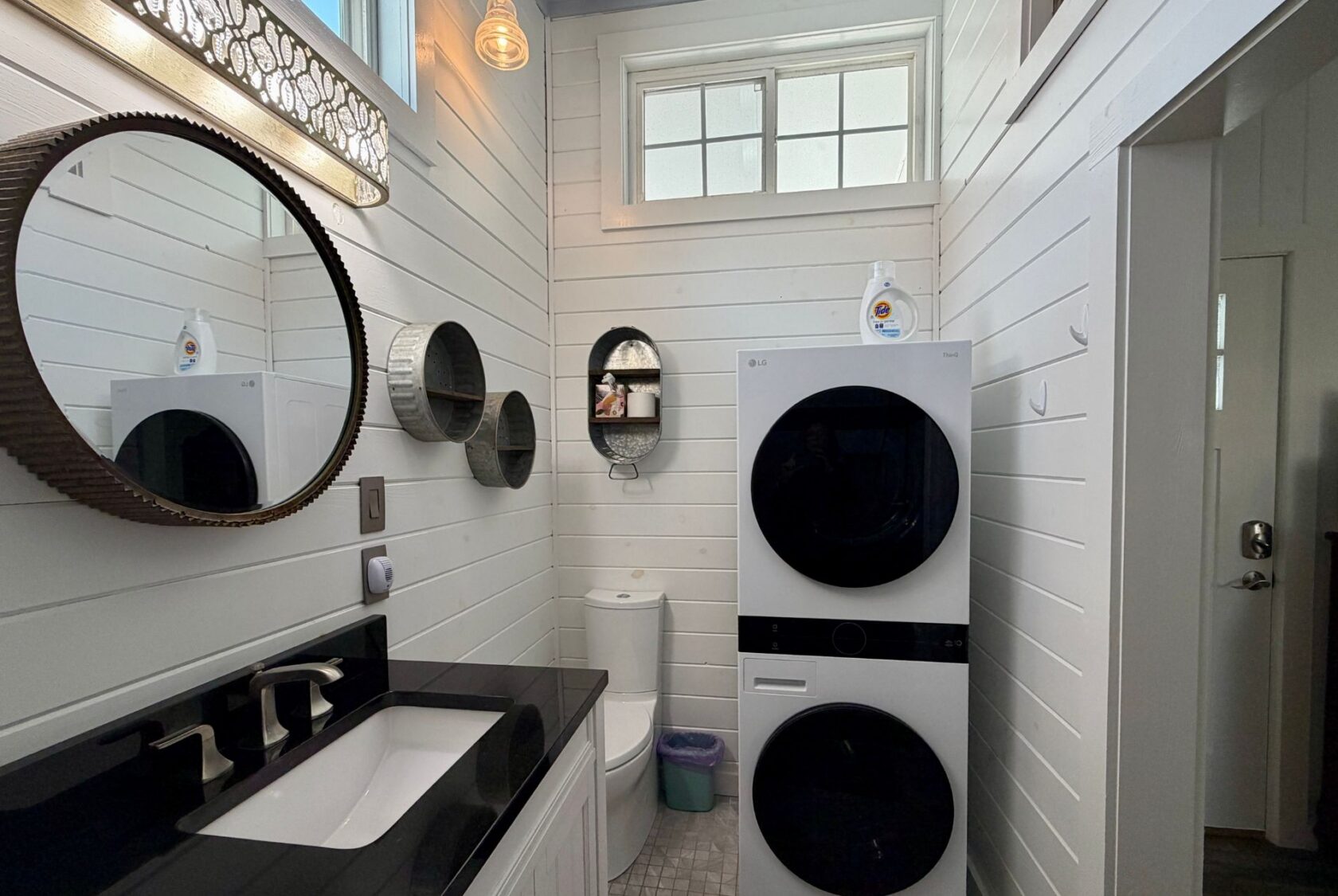 White bathroom at 5 Empire Lane with black sink, round mirrors, and stacked washer and dryer beside the toilet.