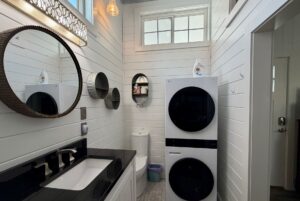 White bathroom at 5 Empire Lane with black sink, round mirrors, and stacked washer and dryer beside the toilet.