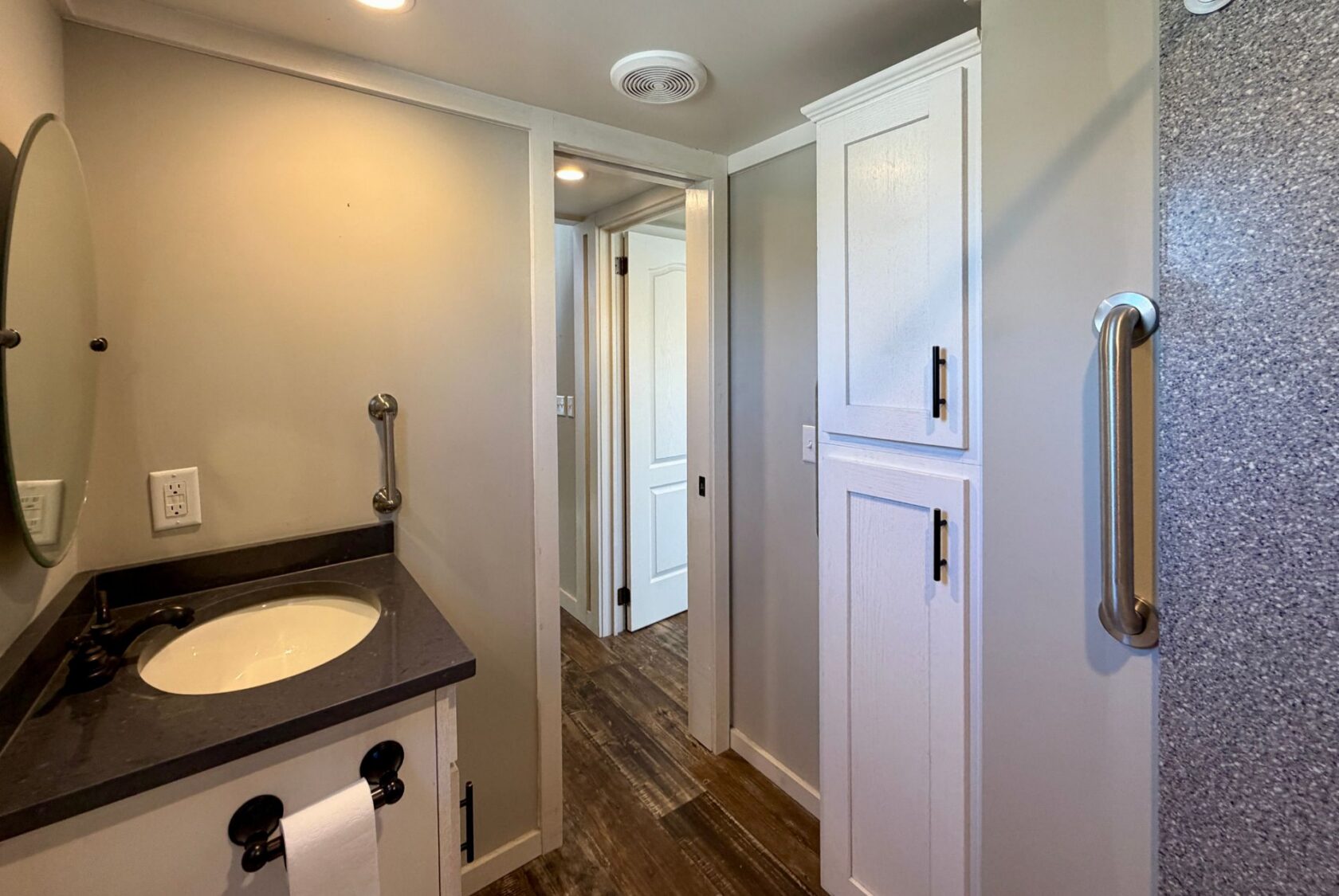 Modern bathroom at 139 Drifting Brook with gray walls, a round mirror, white cabinets, and wood-style flooring.