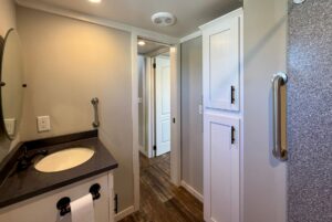 Modern bathroom at 139 Drifting Brook with gray walls, a round mirror, white cabinets, and wood-style flooring.