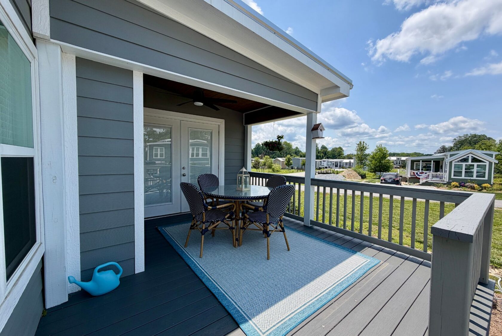 A cozy porch with a table and chairs on a blue rug, overlooking grassy Mount Meadow Lane and nearby houses.