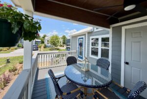 A small porch with a round glass table and chairs overlooks Mount Meadow Lane on a sunny day.