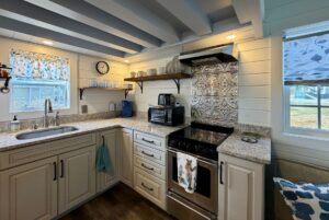 Bright Empire Lane kitchen with white cabinets, patterned backsplash, open shelves, and sunlight through windows.