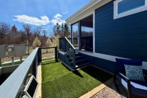 Small patio with artificial grass on Mount Meadow Lane, blue siding, outdoor chair, and stairs to a screened porch.