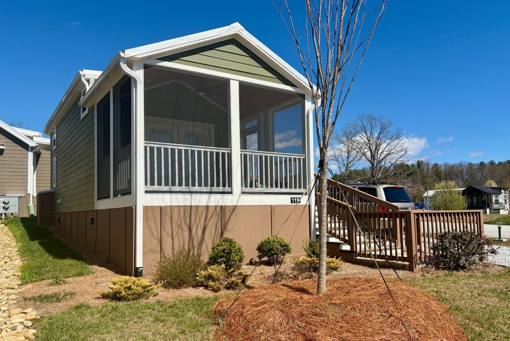 A small green and beige house on Breezy Meadow Lane with a screened porch, ramp, and yard under a blue sky.