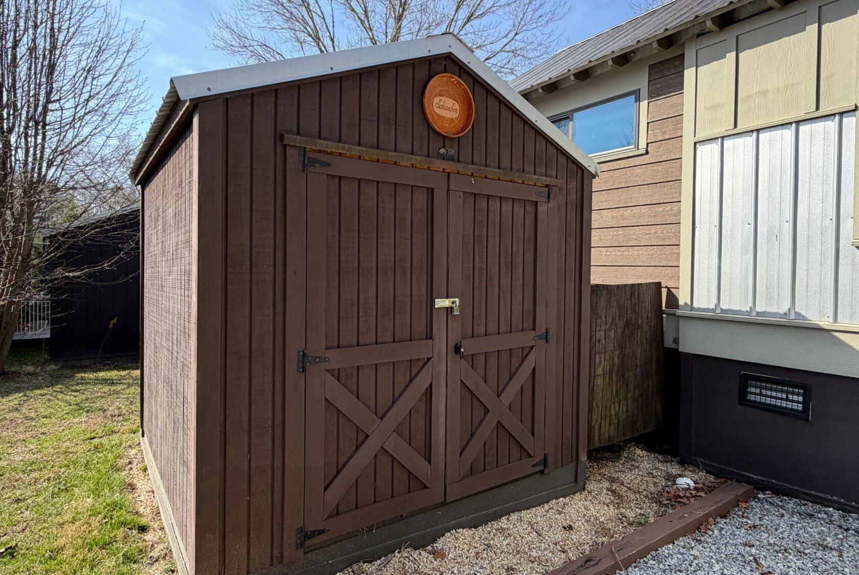 Brown wooden shed with double doors at 31 Rest Awhile Lane, next to a house in a yard with grass and gravel.