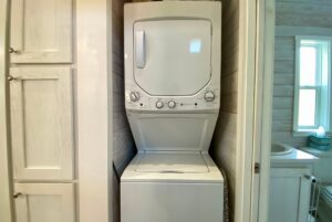 Stacked washer and dryer unit on Easy Lane in a small laundry nook next to a bathroom with a window and sink.