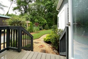 View from a porch with black railings on Just Wandering Lane, overlooking a stone path and lush garden.