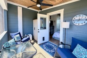 Screened porch on Mount Meadow Lane with blue accents, chairs, glass table, bedroom door, and wall clock at 10:15.