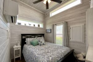 Small, cozy bedroom on Easy Lane with a bed, patterned bedding, two pillows, windows, and light wood paneled walls.
