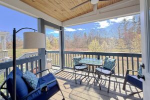 A cozy screened porch on Mount Meadow Lane with a cushioned bench, table, and chairs overlooking a sunny backyard with trees.