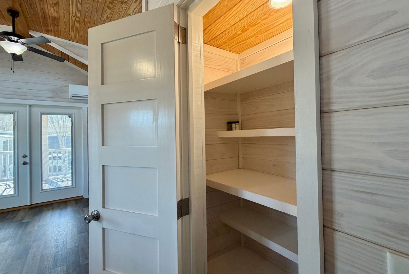 Open white pantry door reveals empty shelves with a few cans in a bright, modern real estate gem on Breezy Meadow Lane.