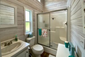 Small bathroom with wood-paneled walls, white fixtures, and a shower—perfect for strolling Easy Lane at home.