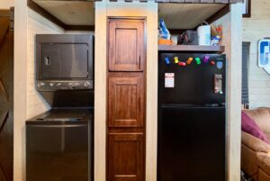 Stacked washer and dryer, wooden cabinet, and black fridge with colorful magnets on Rest Awhile Lane.
