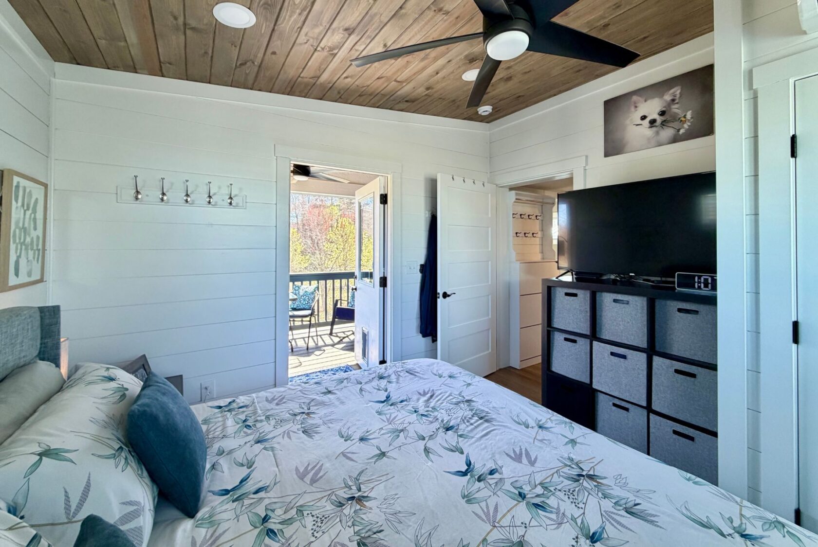 Bright bedroom on Mount Meadow Lane with bed, TV, storage cubes, and balcony access with outdoor seating.