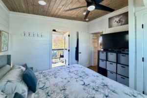 Bright bedroom on Mount Meadow Lane with bed, TV, storage cubes, and balcony access with outdoor seating.