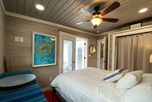 Cozy bedroom on Just Wandering Lane with wood walls, ceiling fan, artwork, and a neatly made bed with white bedding.