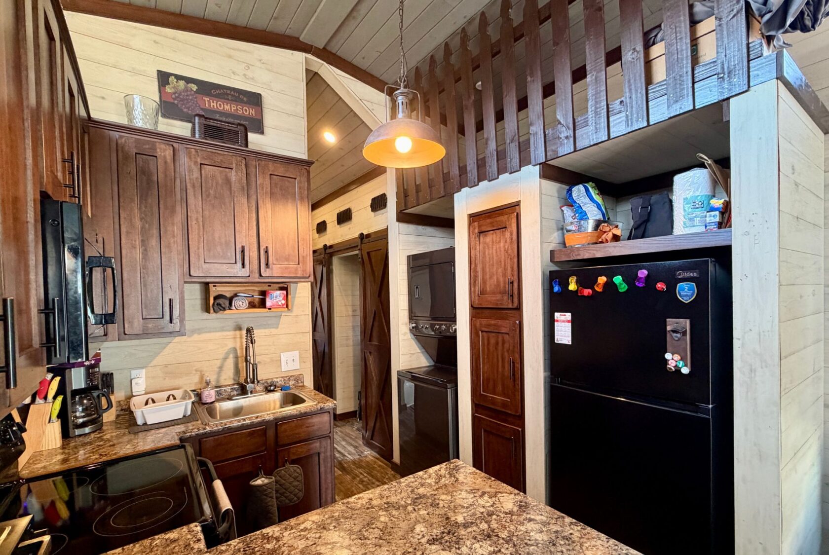 A cozy kitchen at 31 Rest Awhile Lane features wooden cabinets, a black fridge, and a lofted area above a laundry nook.