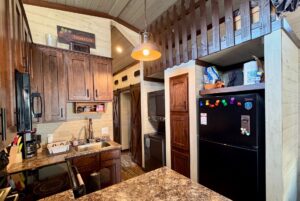A cozy kitchen at 31 Rest Awhile Lane features wooden cabinets, a black fridge, and a lofted area above a laundry nook.